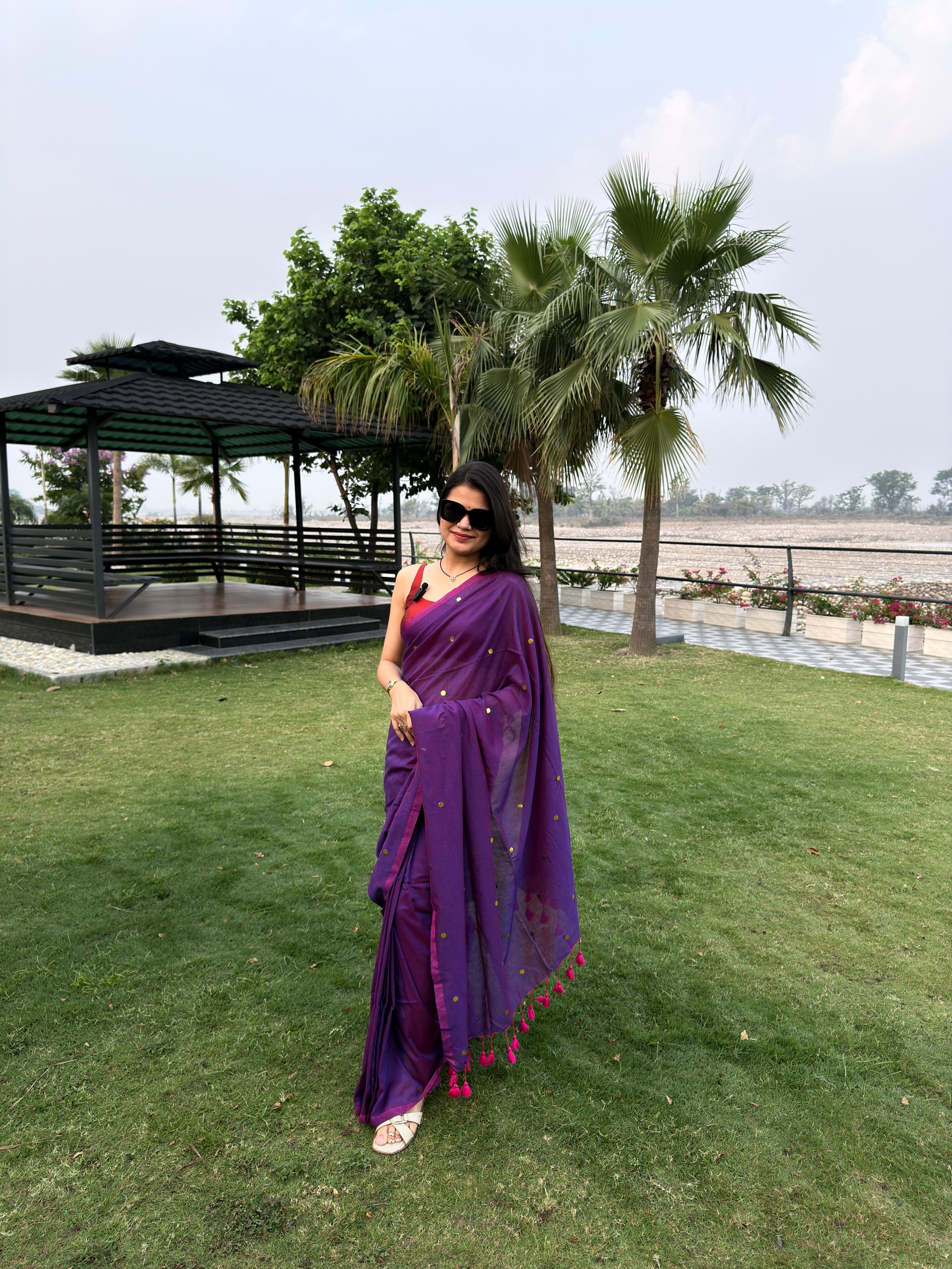 A woman wearing a dual-tone purple chiffon saree embellished with golden sitara sequin buttis, a magenta border, and pink tassels along the pallu.